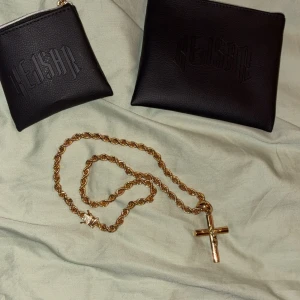 Guldfärgat halsband med kors KEJSAR - Säljer ett snyggt guldfärgat halsband från KEJSAR med tvinnad kedja och ett detaljerat kors som hänge. Kedjan har en cool låsdetalj och korset har en klassisk design med Jesusmotiv. Perfekt accessoar för att lyfta din stil.