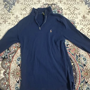 Marinblå half zip tröja Polo Ralph Lauren - Marinblå långärmad tröja från Polo Ralph Lauren med klassisk broderad logga på bröstet. Tröjan har en hög krage och half zip-dragkedja framtill. Perfekt för lager-på-lager och chill stil. Pris kan diskuteras och nån som bor nära haninge kan komma och hämta den då jag behöver pengarna skriv vid intresse.