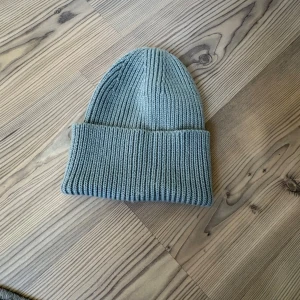 Grön ribbstickad mössa - Snygg grön ribbstickad mössa med bred uppvikt kant. Klassisk modell som sitter skönt på huvudet och passar perfekt till kyliga dagar. Tillverkad i mjukt stickat material som håller värmen och ger en clean look.