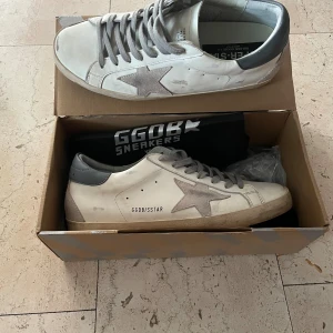 Golden Goose vita sneakers med grå stjärna - Golden Goose sneakers i vitt skinn med grå mockadetaljer och ikonisk stjärna på sidan. Grå snörning och grå hälkappa ger en clean men edgy look. Platt sula och rund tå.