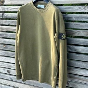 Olivgrön långärmad tröja Stone Island - Olivgrön långärmad tröja från Stone Island med klassisk rund hals och ikonisk logotyp-patch på vänster ärm. Tröjan är i mjuk bomull och sick 8/10