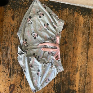 Disney Minnie Mouse grå shorts - Grå shorts från Disney med gulligt Minnie Mouse-tryck i svart och rosa. Mjuk resår i midjan och rosa snörning framtill. Perfekta för chill dagar eller som pyjamasshorts. Tillverkade i bomull för en skön känsla.