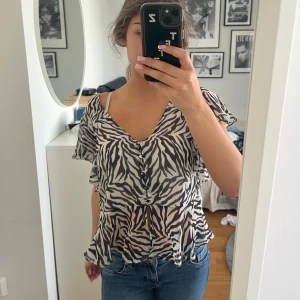 Zebramönstrad blus med volang Bubbleroom - Säljer en luftig zebramönstrad blus med v-ringning och knappar framtill. Toppen är från Bubbleroom i storlek 38!