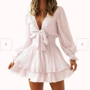 Ljusrosa kortklänning från Design By Amor - Supersöt ljusrosa kortklänning från Design By Amor med volangkant, djup v-ringning och knyt framtill. Klänningen har långa puffärmar och är tillverkad i ett lätt, flowy material som ger en romantisk vibe. Perfekt för dig som vill sticka ut med en feminin look. (Skriv för fler bilder och frågor💕)