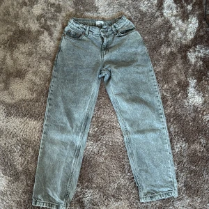 Grå jeansbyxor från Grunt - Säljer ett par grå jeansbyxor från Grunt med klassisk femficksdesign och raka ben. Byxorna har hög midja och är tillverkade i ett slitstarkt jeanstyg. Perfekta för dig som gillar en enkel och tidlös look.