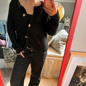 Svart stickad kofta med guldknappar - Mysig svart stickad kofta med snygga silver knappar framtill. Koftan har lång ärm och en lite lösare passform, perfekt att slänga på sig över ett linne eller t-shirt. Enkel och stilren design som funkar året runt.