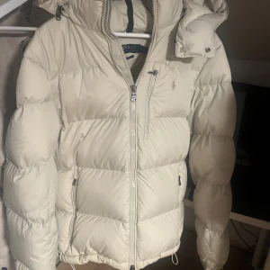 Beige dunjacka Polo Ralph Lauren M - Beige Ralph lauren jacka. Går inte att få tag på längre. Slutsåld överallt, helt ny modell. Nypris 6000 kr på zalando där allt är slut och jackan bara ökar i pris. Köpte jackan som ett spontan köp i Göteborg på avenyn i somras och har aldrig använt den. För de har varit sommar. Skriv om ni har funderingar MVH Albin 