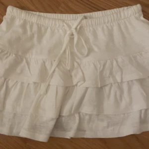 Vit volangkjol med knytband - Supersöt vit kortkjol med volanger och knytband i midjan. Storlek S men eftersom midjan går att dra åt är det lite justerbart❣️Aldrig använd så den är som ny