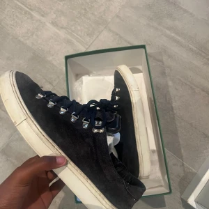 Svarta mocka sneakers från Diemme - Säljer ett par svarta sneakers från Diemme med snygg mocka-yttermaterial och vita platta sulor. Skorna har metallöglor och mörkblå snörning som ger en cool outdoor-vibe. Perfekt för dig som gillar stilrena och unika detaljer på dina skor.