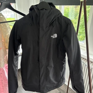 The North Face jacka - Säljer en svart jacka från The North Face. Jackan har huva, dragkedja framtill och en bröstficka med dragkedja. Perfekt för blåsiga och kyliga dagar. Enkel och stilren design med logga på bröstet och ryggen. Modellen är Freedom insulated jacket W TNF black. Använd endast två gånger förra vintern. Ordinarie pris 3 499kr.