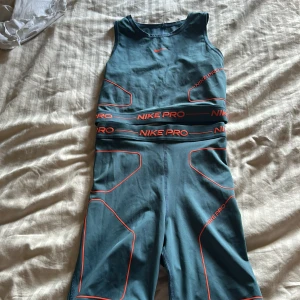 Nike Pro blå träningsett  - Nike Pro träningsett i blått med orange detaljer och logga. Tight passform och hög midja, tillverkade i mjukt och stretchigt syntetmaterial som andas. Snygga kontrastlinjer och bred resår med Nike Pro-tryck gör dem perfekta för gymmet eller sport. Funkar också som en S 