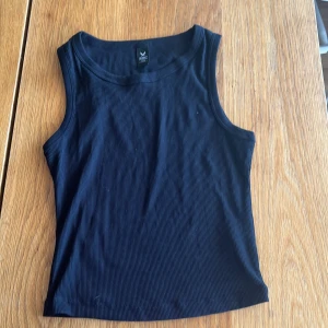 Svart ribbad linnetopp från SOC - Säljer en svart ribbad linnetopp från SOC. Toppen är ärmlös med rund halsringning och har en tight passform. Perfekt att matcha med jeans eller shorts för en clean och enkel look.