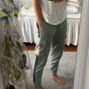 Gröna cargopants från Nike - Snygga ljusgröna cargopants från Nike med svarta detaljer längs sidorna och stor ficka på båda sidorna av benet. Byxorna har elastiska muddar vid benslut och är gjorda i mjukt bomullsmaterial. Perfekta för chill eller streetwear. Dock så har byxorna två fläckar som knappt syns! En vid högra ben fickan och en vid ankeln. Men som sagt syns inte om man inte kollar riktigt nära. 