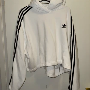 Vit Adidas hoodie med svarta ränder XL - Säljer en vit hoodie från Adidas i storlek XL. Tröjan har klassiska svarta ränder längs ärmarna, Adidas-logga på bröstet och huva. Oversized och skön passform, perfekt för en chill och sportig look.