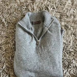 Grå halvziptröja från Oscar Jacobson - Snygg grå stickad tröja från Oscar Jacobson med ribbad krage och half zip-dragkedja. Perfekt för lager-på-lager och chill stil. Långärmad och i mjukt material som känns skönt mot huden.