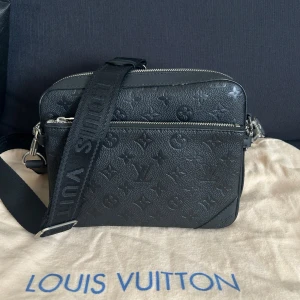 Svart axelväska  - Snygg svart axelväska. Väskan har justerbar axelrem med logga, silverfärgade dragkedjor och flera fack för smart förvaring. 