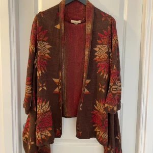 Mönstrad kofta från Ralph Lauren - Säljer en sjukt snygg kofta från Denim & Supply Ralph Lauren i brunt, rött och orange. Koftan har ett unikt etnoinspirerat mönster, öppen front och vida ärmar. Materialet är 100% bomull och den är perfekt för lager på lager under höst och vinter.