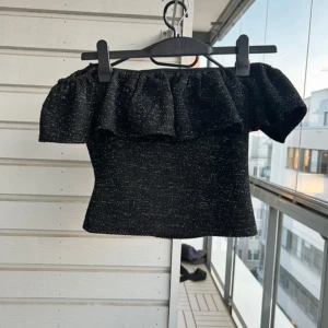 Svart glittrig offshoulder topp H&M - Säljer en svart glittrig offshoulder topp från H&M med volang upptill. Toppen är croppad och har en snygg figurnära passform. Perfekt för dig som vill sticka ut med lite extra glitter och volym på axlarna. stl s! 
