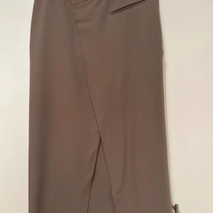 Beige omlott kostymbyxor - Snygga beige kostymkjol med omlott-detalj i midjan . Kjol  har hällor för bälte och fickor både fram och bak. Perfekta för en clean och stilren look. Materialet känns mjukt och har en lätt stretch.