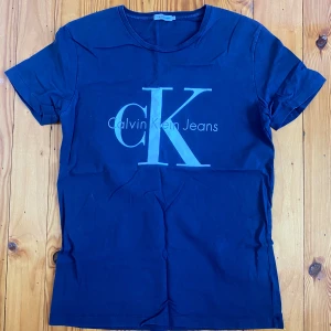 Blå Calvin Klein Jeans t-shirt - Snygg marinblå t-shirt från Calvin Klein Jeans med stort CK-logga tryckt på bröstet. Klassisk rund halsringning och korta ärmar. Perfekt för en clean och stilren look.