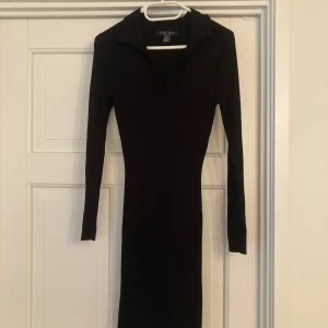 Svart ribbad långklänning från Amisu - Svart långklänning från Amisu med ribbad struktur och lång ärm. Klänningen har en snygg v-ringning med krage och figurnära passform som ger en clean och stilren look. Perfekt för dig som gillar minimalistisk stil och klassisk .Perfekt om du vill klä upp dig enkelt. 