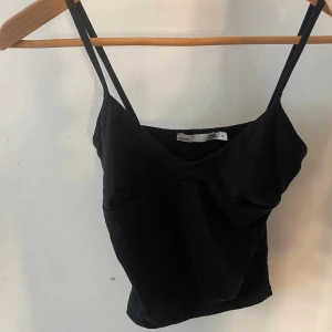 Svart linnetopp från 157, XS - Säljer en svart linnetopp från 157 i storlek XS. Toppen har smala axelband och en lätt v-ringad skärning framtill. Enkel och stilren design som passar perfekt till jeans eller kjol. Materialet känns mjukt och följsamt mot huden.
