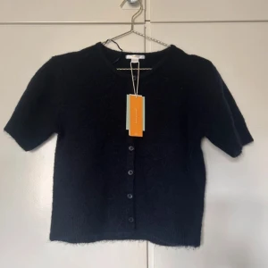  kofta från Gina Tricot - Kortärmad svart kofta från Gina Tricot med rund halsringning och knappar framtill. Koftan är stickad och har en mjuk, fluffig känsla. Perfekt att styla över ett linne eller t-shirt för en chill look. Storlek 158/164❤️så xxs ungefär 