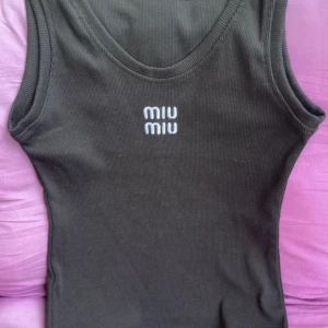 Svart ribbad linnetopp från Miu Miu - Svart ribbad linnetopp från Miu Miu med broderad logga framtill. Modellen är ärmlös med rund halsringning och har en slim passform. Materialet är mjuk bomull som känns skönt mot huden. Perfekt för dig som gillar stilrena och lyxiga basics. Köpt härinne för 500 kronor vet inte om den är äkta. Storlek L men skulle säga den passar en S 