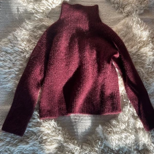 Vinröd stickad tröja - Säljer en vinröd stickad polotröja med hög krage och långärmad design. Tröjan har en mysig och mjuk känsla, perfekt för kyliga dagar. Färgen är djup vinröd som ger en snygg struktur. Passar dig som gillar klassisk stil med en twist.