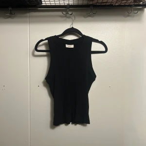 Svart ribbad linnetopp Gina Tricot - Säljer en svart ribbad linnetopp från Gina Tricot, basically basics-kollektionen. Toppen är ärmlös med rund halsringning och har en tight passform. Materialet är stretchigt och bekvämt, perfekt för att styla med jeans eller kjol.