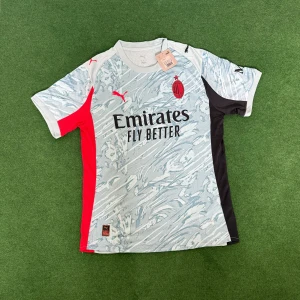 AC Milan 25/26 fotbollströja Puma - AC Milan matchtröja från Puma med coolt abstrakt mönster i ljusgrått och vitt, röda och svarta paneler på sidorna och ärmarna. Röd Puma-logga och klubbmärke på bröstet, samt Emirates Fly Better-tryck. Tillverkad i lätt och ventilerande polyester.