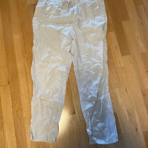 Beiga linnebyxor från H&M med snörning - Luftiga beiga linnebyxor från H&M med relaxed fit och elastisk midja med snörning. Perfekta för varma dagar och chill vibes. Byxorna har raka ben och är tillverkade i ett mjukt linnematerial som känns svalt mot huden.