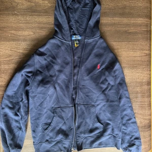 Svart hoodie från Polo Ralph Lauren XL - Svart hoodie från Polo Ralph Lauren i storlek XL (barnstolekar så passar typ 165-175). Klassisk design med dragkedja, huva och två stora fickor framtill. Broderad röd logga på bröstet. Mjuk insida och skön passform, perfekt för chill dagar. Ingen aning varför den ser så rynkig ut den är i bra skick💔🙏