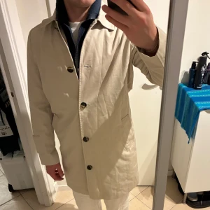 Beige rock från Dobber, storlek S - Stilren beige rock från Dobber med klassisk krage och knäppning framtill. Jackan har raka linjer, två fickor och snygga knappar. Perfekt för dig som gillar en clean och tidlös look. Materialet är bomull och passformen är normal. Sitter som xs