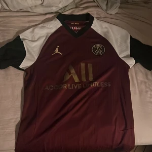 PSG Neymar Jr Jordan fotbollströja M 2020/21 tredje - Snygg PSG fotbollströja i samarbete med Jordan, Neymar Jr #10 på ryggen. Tröjan är vinröd med svarta och vita detaljer, guldiga loggor och tryck. Sällan använd 