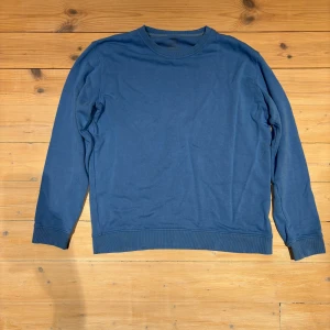 Blå långärmad Resteröds sweatshirt i bomull - En enkel och stilren blå sweatshirt med rund hals och långa ärmar. Tröjan har ribbade muddar vid ärmslut och nederkant, vilket ger en schysst passform. Perfekt för dig som gillar en clean look och mjuka material. Lite liten i storleken så kanske mer av en Large tröja.