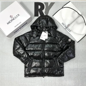 Svart pufferjacka från Moncler - Svart pufferjacka från Moncler med glansig finish och huva. Jackan har dragkedja framtill, två sidofickor med dragkedja och Moncler-logga på ärmen. Materialet är syntet och dun, perfekt för kalla dagar. Snygg och stilren design som sticker ut.