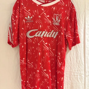 Liverpool retro fotbollströja Adidas - Riktigt snygg röd retro Liverpool FC fotbollströja från Adidas med klassiskt tryck 'Candy' på bröstet och nummer 2 på ryggen, numret som Glenn Hysén bar i Liverpool. Tröjan har ett vitt abstrakt mönster, korta ärmar och klubbens emblem på bröstet. 