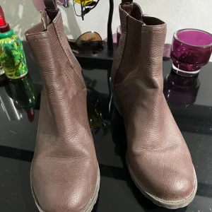 Bruna chelsea boots från Vox Shoes - Snygga bruna chelsea boots från Vox Shoes i skinn med grov sula och låg klack. Elastiska paneler på sidorna gör dem enkla att ta på och av. Rund tå och klassisk siluett . Perfekt för höst och vinter.
