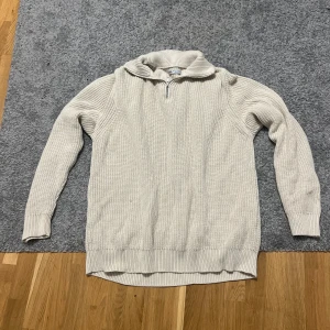 Beige stickad half zip-tröja från Zara - Säljer en beige stickad tröja från Zara med half zip och hög krage. Tröjan har lång ärm och ribbade muddar, perfekt för lager på lager. Enkel och clean design som funkar till allt.