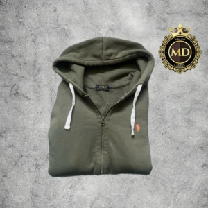 Polo Ralph Lauren hoodie  - Olivgrön hoodie från Polo Ralph Lauren med dragkedja, vita snören och klassisk broderad logga i orange på bröstet. Mjuk bomullskänsla, kängurufickor och huva. Perfekt för chill dagar och enkel att matcha med jeans eller joggers. Tröjan är i mycket bra skick. Storleken på hoodien är m men kan passa s! Skirv vid frågor eller mer bilder⚜️