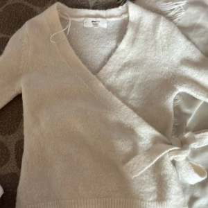 Beige omlottkofta från Gina Tricot XS - Supermjuk beige omlottkofta från Gina Tricot i ullblandning. Koftan har lång ärm, ribbade muddar och knyt i sidan för en snygg passform. Perfekt för lager-på-lager och chill vibes.