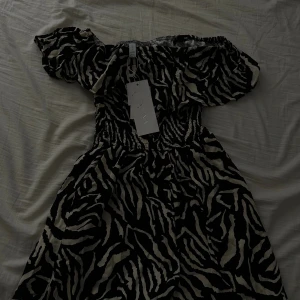 Zebramönstrad offshoulder klänning Amisu - Helt nya!! Prislapp kvar  Pris💰💰100 styck 150  för båda  kort offshoulder klänning från Amisu med zebramönster. Klänningen har smockad midja och volang upptill, vilket ger en snygg och bekväm passform. Finns i två färger: svart/vit och orange/vit. Perfekt för dig som gillar att sticka ut med coola mönster. Perfekt inför sommaren 