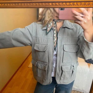 Grön cargo jacka från H&M - Säljer en grön cargo jacka från H&M med fyra stora fickor framtill och en cool utility-vibe. Jackan har dragkedja, klassisk krage och är tillverkad i bomull. Perfekt att slänga över en t-shirt för en chill look. Säljer då den inte kommer till användning längre