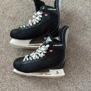 Skridskor Head S2 - Snygga svarta skridskor från Head S2 med vita och svarta mönstrade snören. De har robust design, silverdetaljer och X Lite-blad. Perfekta för isen med bekväm passform och klassisk look.
