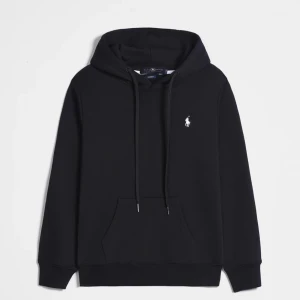 Svart hoodie från Polo Ralph Lauren - Svart hoodie från Polo Ralph Lauren med klassisk huva och snörning. Tröjan har en vit broderad logga på bröstet och en stor magficka framtill. Mjuk bomullskvalitet och långärmad modell som är perfekt för chill dagar.