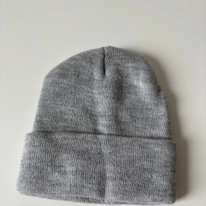 Ljusgrå stickad mössa - En enkel och stilren grå stickad mössa med bred uppvikt kant. Perfekt för kalla dagar och passar till de flesta outfits. Mjuk och skön känsla, klassisk form utan synliga loggor eller detaljer. Helt ny.