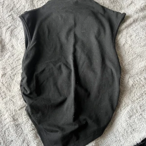 Svart ärmlös linnetopp - Säljer en svart ärmlös linnetopp med högre hals och spetsig nederkant. Toppen har en clean och enkel design som passar perfekt till jeans eller kjol. Materialet känns mjukt och stretchigt, vilket gör den bekväm att bära hela dagen.