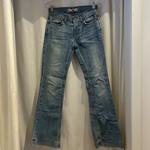 Bootcut jeans från Fornarina - Snygga ljusblå bootcut jeans från Fornarina med klassisk femficksdesign och slitna detaljer. Jeansen har låg midja, gylf med knapp och dragkedja samt dekorativa sömmar på bakfickorna. Perfekta för en avslappnad och trendig look. Innerbens längd:77 cm