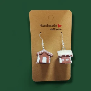 Handgjorda pepparkakshus örhängen - Supergulliga handgjorda örhängen formade som små pepparkakshus med vita detaljer som ser ut som snö och glasyr. Perfekta för dig som vill sticka ut med ett lekfullt och juligt smycke. Hängena är bruna och vita och har silvriga krokar.